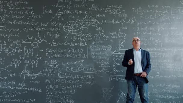 Thoughtful man walking near chalkboard thinking then writing formulas finding solution — Stockvideo