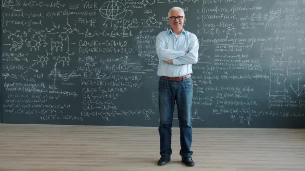 Portrait of cheerful man standing in class with chalkboard wall smiling looking at camera — Stockvideo