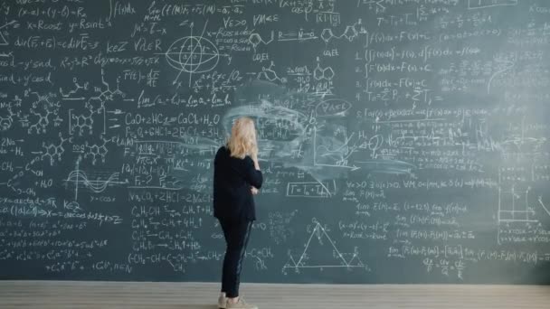 Time-lapse of female professor walking near chalkboard looking at formulas thinking — Stockvideo