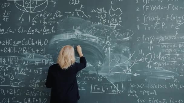 Mujer adulta profesora escribiendo fórmulas en pizarra hablando clase de enseñanza en la escuela — Vídeo de stock