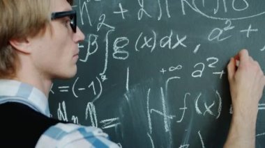 Kara tahtaya formüller yazan genç matematikçi ciddi bir yüzle çalışıyor.
