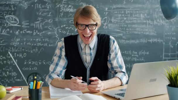 Portret van een gelukkige jongeman gekke wetenschapper lachend in de klas aan het bureau kijkend naar camera — Stockvideo