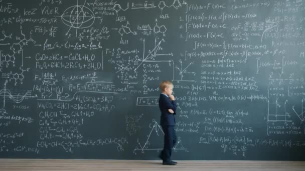 Przemyślany dzieciak spacerujący koło ściany tablicy w klasie myślący o nauce — Wideo stockowe