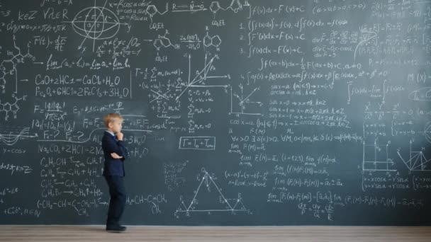 クラスを歩く式を持つ黒板を見て科学について考える小さな天才 — ストック動画