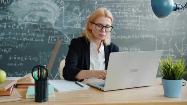 Egyetemi professzor laptopot használ, majd jegyzetel az asztalnál az osztályban. — Stock videók