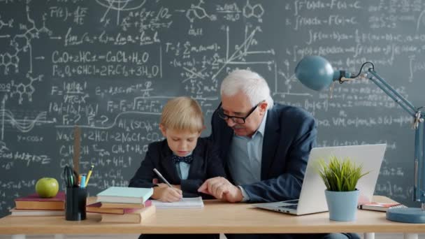 Professor caring grandfather teaching little boy grandson in class talking writing — Stockvideo