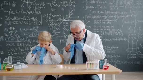 Niño y maestro poniéndose guantes de goma antes de experimentos químicos — Vídeo de stock