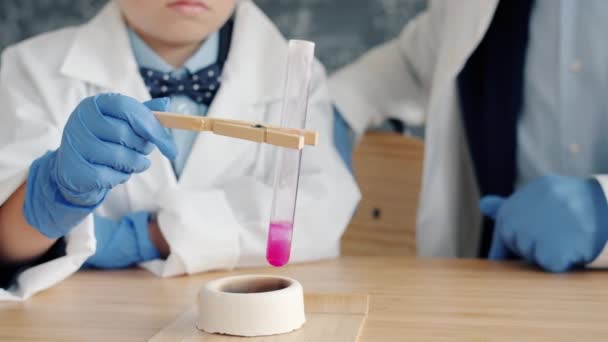 Nahaufnahme einer chemischen Reaktion: Kind und Lehrer erhitzen Glasrohr über Brenner — Stockvideo