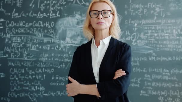 Portrait of serious smart lady professor in classroom with formulas on chalkboard — ストック動画