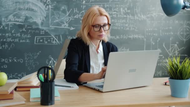 Mature woman using laptop in class working online typing sitting at desk alone — Stockvideo