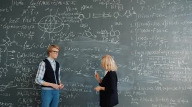 University professor teaching handsome guy student writing formulas on chalkboard