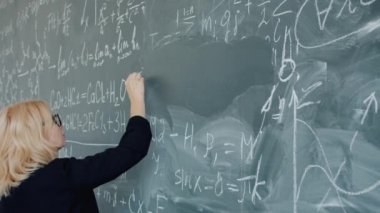 Slow motion of female chemistry teacher serious woman writing formulas on chalkboard