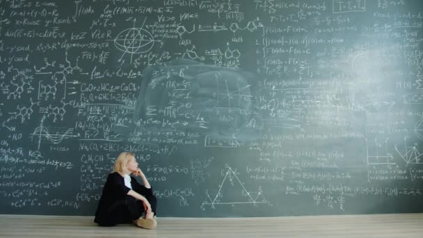 Portrait of puzzled female scientist sitting on floor near chalkboard talking gesturing — Stockvideo