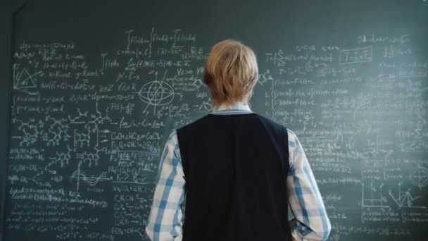 Portrait of intelligent guy in casual clothing walking to chalkboard writing formulas — Stock video