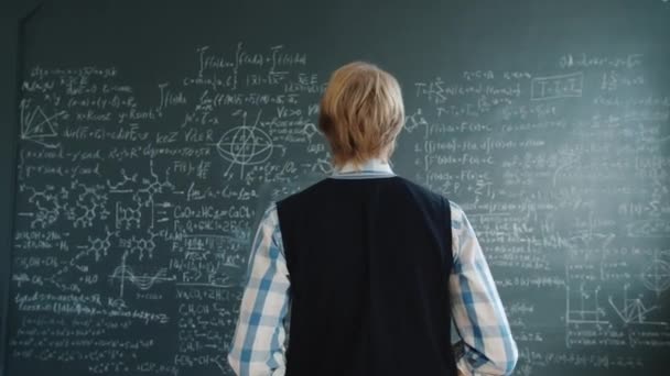 Portrait of intelligent guy in casual clothing walking to chalkboard writing formulas — ストック動画