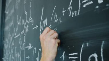 Close-up slow motion of maths student writing formulas on blackboard indoors