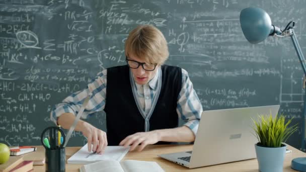 Crazy man scientist using laptop writing in notebook expressing positive emotions — Stock video