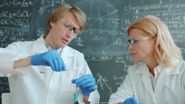 Químicos femeninos y masculinos trabajando en laboratorio con tubos de ensayo ocupados con el experimento — Vídeo de stock