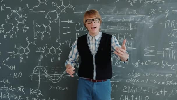 Portrait of handsome guy maths teacher talking looking at camera near chalkboard — Stock video