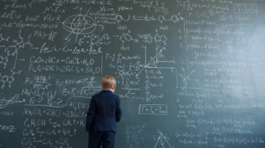 Slow motion of intelligent child writing formulas on blackboard wall in college