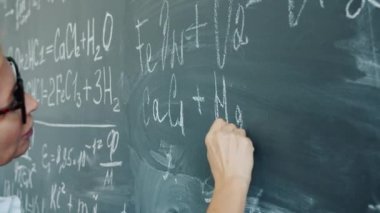Close-up of womans hand writing formulas on blackboard in college classroom