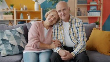 Portrait of couple senior man and woman smiling looking at camera at home on sofa