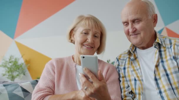 Senior couple using smartphone swiping discussing content relaxing in house together — Stockvideo