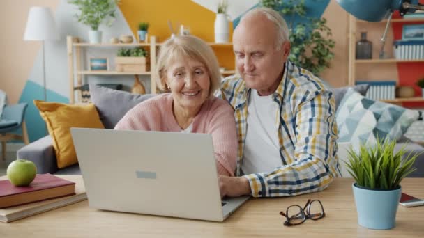 Ouderen paar met behulp van computer thuis praten typen genieten van internet content — Stockvideo