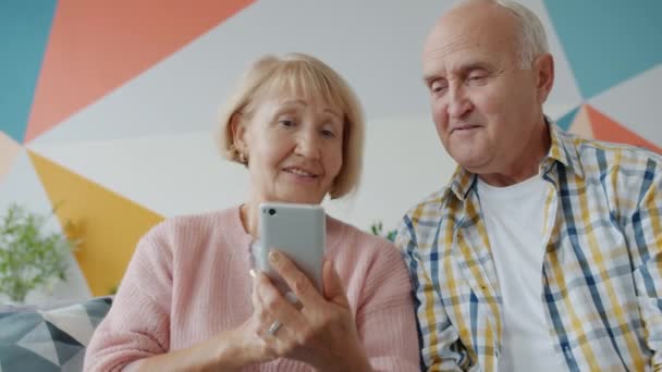 Pareja de ancianos hombre y mujer usando la pantalla táctil del teléfono inteligente hablando en casa — Vídeo de stock