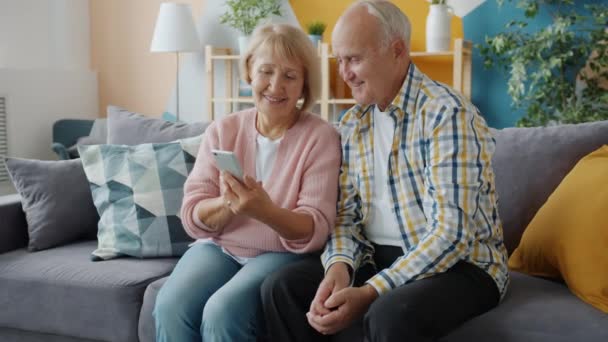 Senioren man en vrouw met behulp van smart phone in appartement praten vegen scherm — Stockvideo
