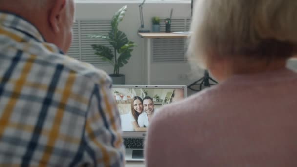 Щасливі старші батьки розмовляють з молодою парою, використовуючи ноутбук, який показує великі пальці вдома — стокове відео