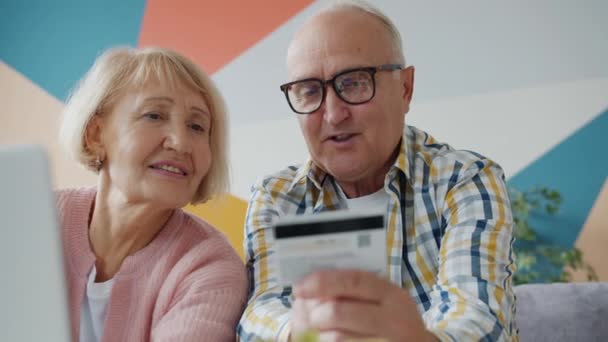 Пожилой мужчина и женщина делают покупки онлайн с помощью банковской карты с помощью ноутбука дома — стоковое видео