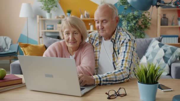 Pria dan wanita senior dengan laptop tersenyum sambil memandang ke layar. — Stok Video