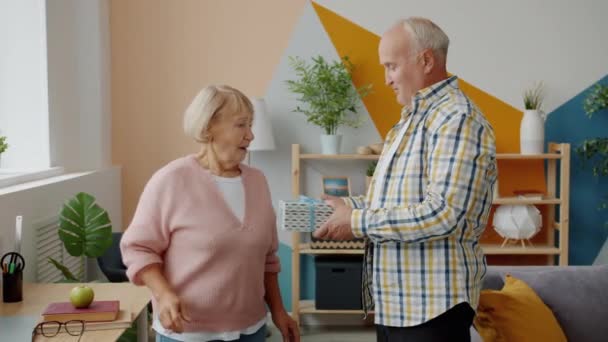 Äldre kvinna får presentförpackning på semester från kärleksfull man i modern lägenhet — Stockvideo