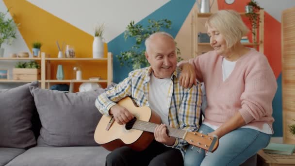 Nyugdíjas pár gitározik és énekel élvezi a romantikus napot otthon — Stock videók
