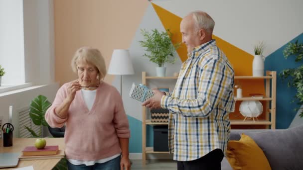 Nyugdíjas férfi lassú mozgása, aki ajándékdobozt ad a boldog asszonynak szeretett feleségének otthon. — Stock videók
