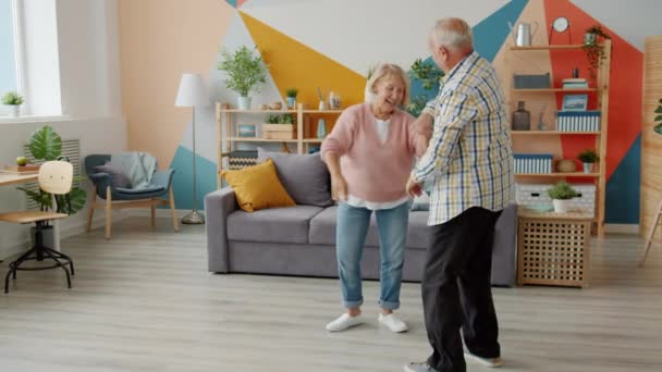 Медленное движение веселых пожилых людей, танцующих дома, улыбающихся, смеющихся, веселящихся — стоковое видео