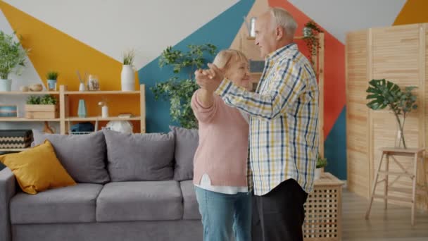 Movimento lento do homem sênior e da mulher dançando em casa de mãos dadas desfrutando de música — Vídeo de Stock
