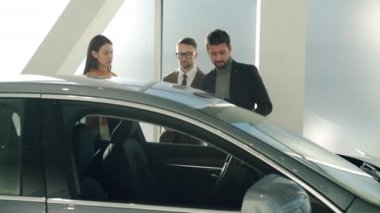Man and woman buyers talking to car dealership manager discussing automobile