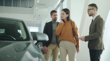 Young family purchasing automobile in car dealership talking to sales manager