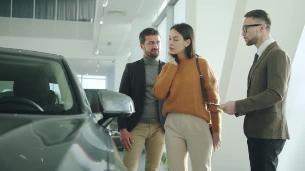 Jeune famille achetant une automobile dans un concessionnaire automobile parler au directeur des ventes — Video