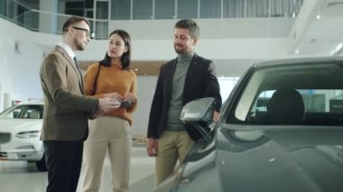 Joyful young family choosing new automobile in car showroom talking to manager