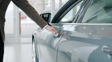 Close-up shot of male hand opening car door in luxury auto dealership looking inside