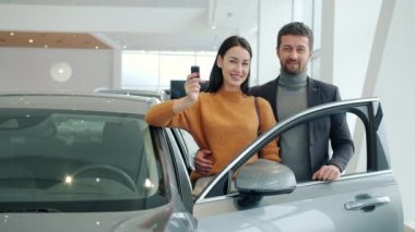 Portrait of happy young couple smiling standing beside expensive car in showroom