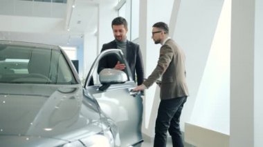 Salesman opening car door for buyer selling new automobile in dealership