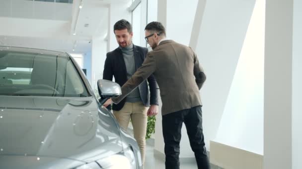 Salesman opening car door for buyer selling new automobile in dealership — Stok video