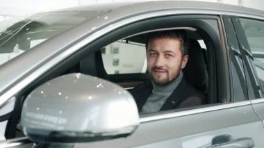 Portrait of bearded guy new car owner sitting inside beautiful automobile smiling
