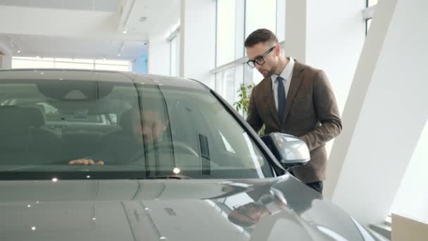Sales manager talking to client sitting in car in showroom choosing automobile — Αρχείο Βίντεο