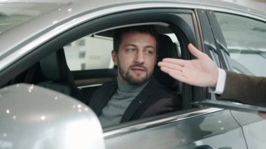Car dealership client getting key fob from sales manager sitting inside new car