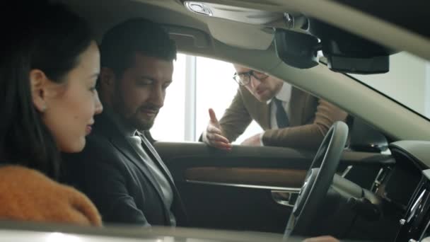 Sonriendo joven pareja dentro de coche nuevo hablando con gerente de ventas en la concesionaria — Vídeos de Stock